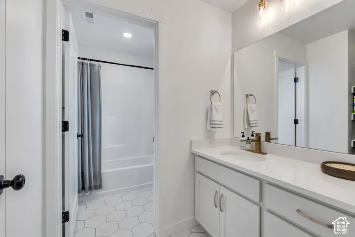 Bathroom featuring a white vanity with a composite countertop, undermount sink, brass-finish faucet, wall-to-wall mirror, and hexagonal floor tile