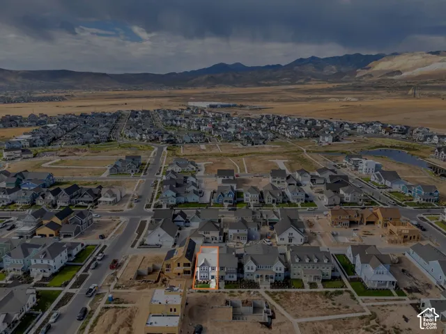 Aerial perspective of a multi-story residence featuring a gray exterior with gabled roof lines, set against a backdrop of prominent mountain ranges