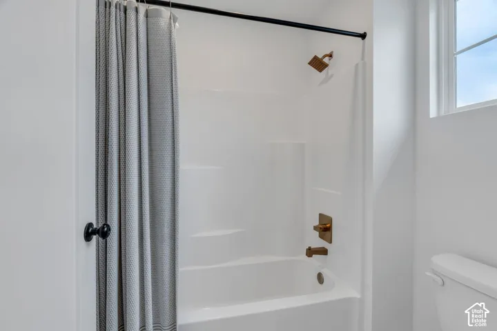 Bathtub and shower combination featuring a white surround, brass-finish fixtures, a matte black shower rod, and an integrated window