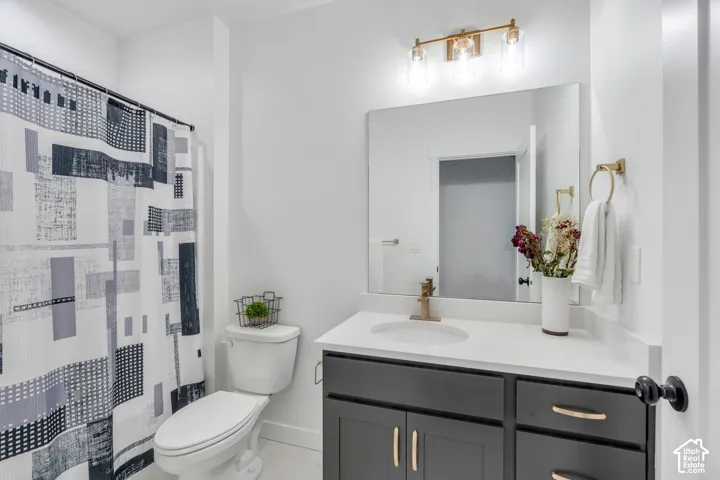 Bathroom featuring a dark gray vanity with gold hardware, a white countertop, a rectangular mirror, and a gold-finish light fixture