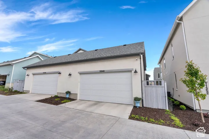 Modern stucco exterior featuring two garage doors, dark shingle roofing, and contemporary exterior lighting fixtures