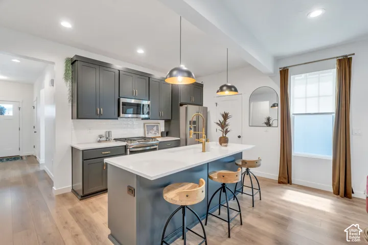 Kitchen featuring dark cabinetry, white countertops, a central island with a gold-tone faucet, recessed lighting, and wood-finish flooring