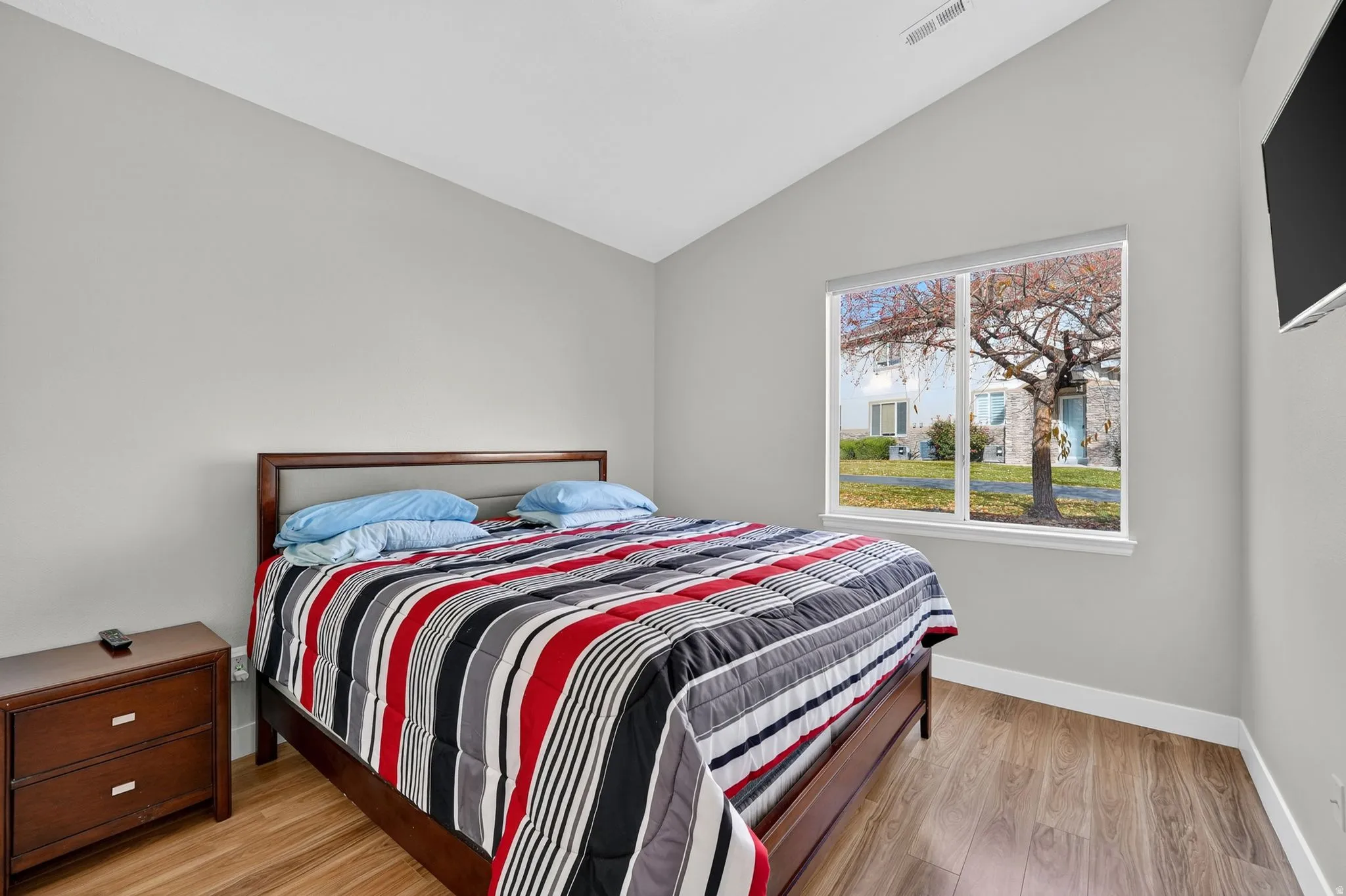 Bedroom with vaulted ceiling, wood-finish flooring, and a large window