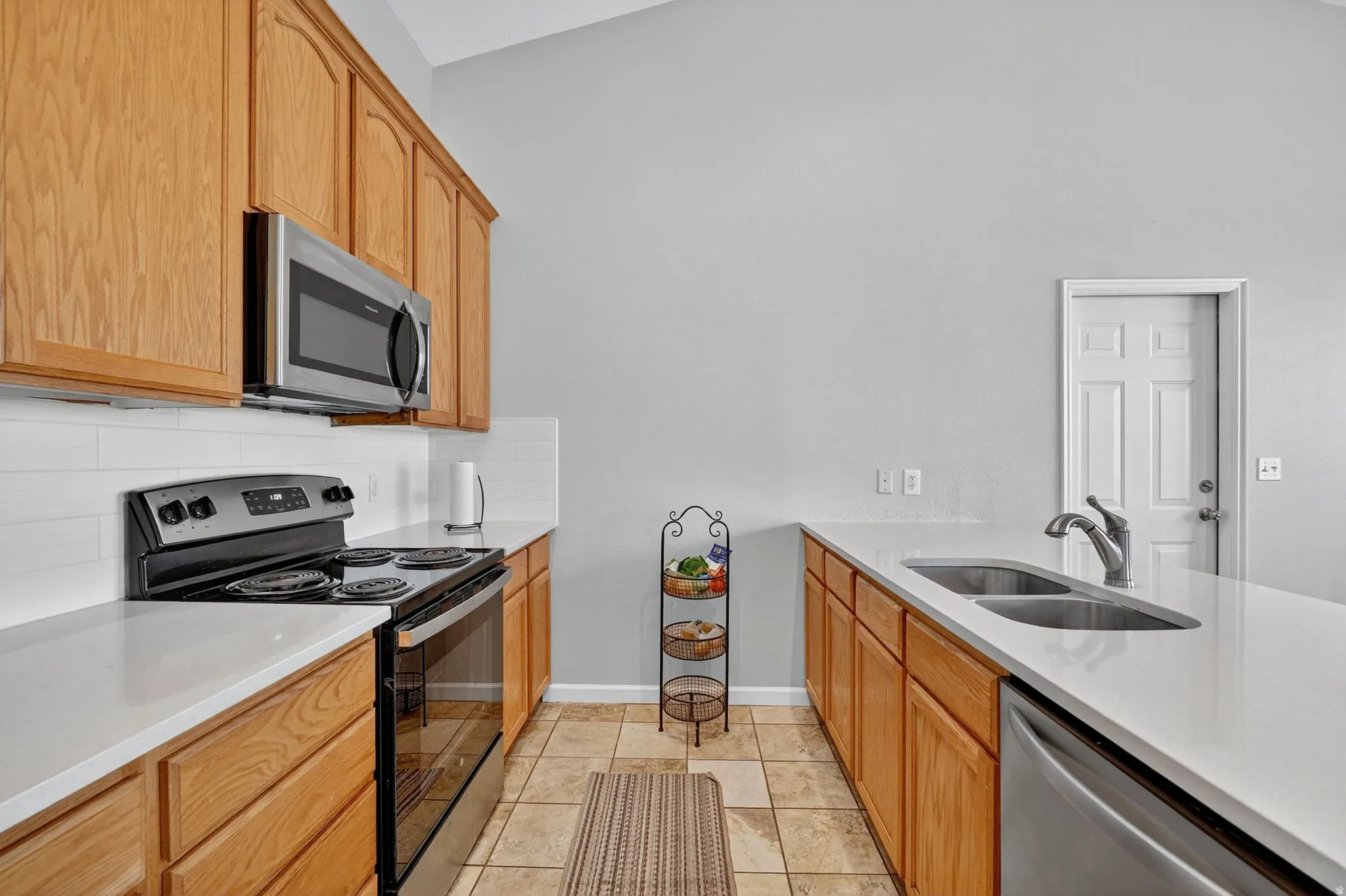 Kitchen featuring light wood cabinetry, white countertops, tile flooring, and stainless steel appliances including a microwave, range, and dishwasher