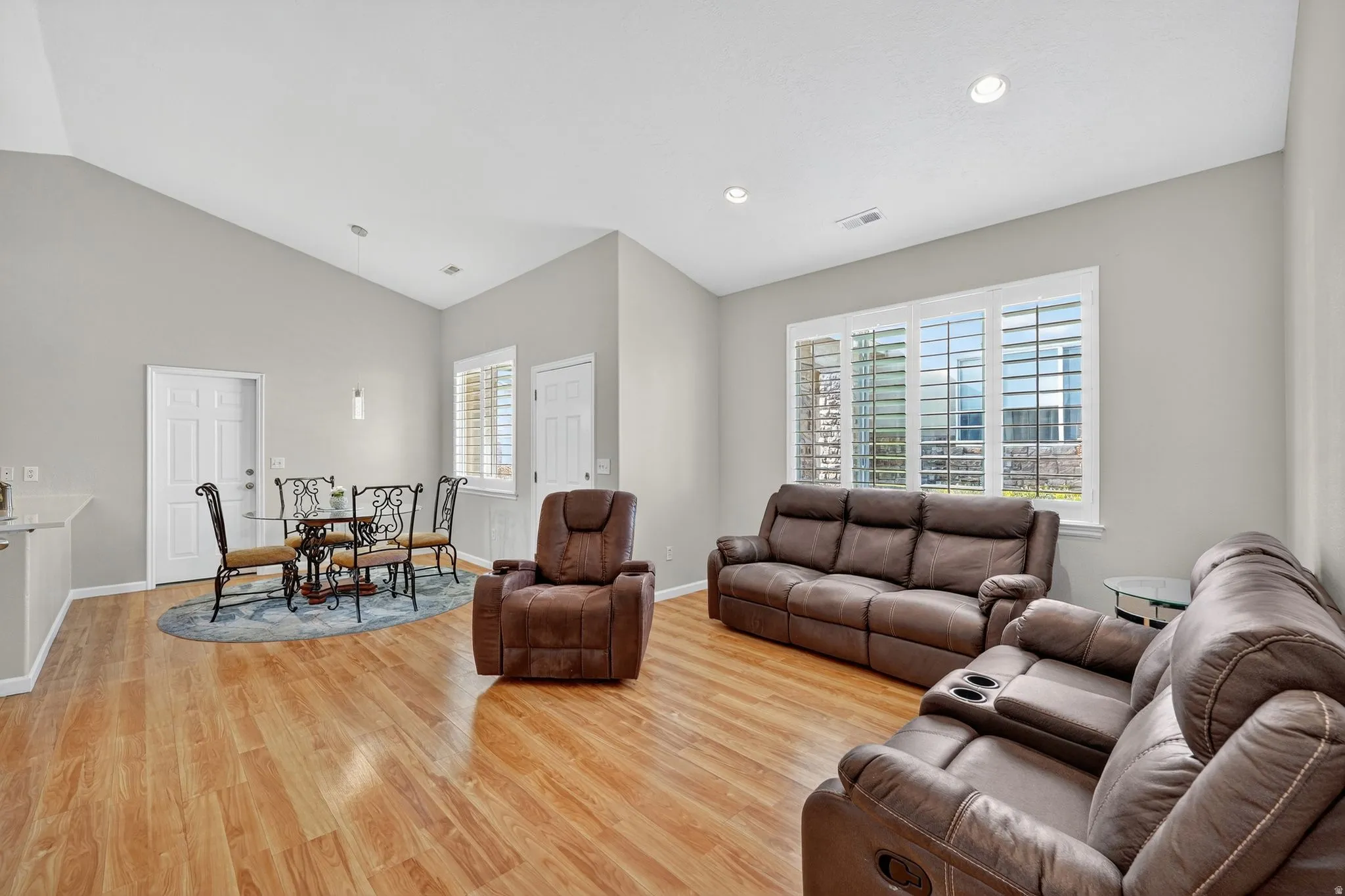 Open concept living and dining area featuring wood-finish flooring, vaulted ceilings, and recessed lighting