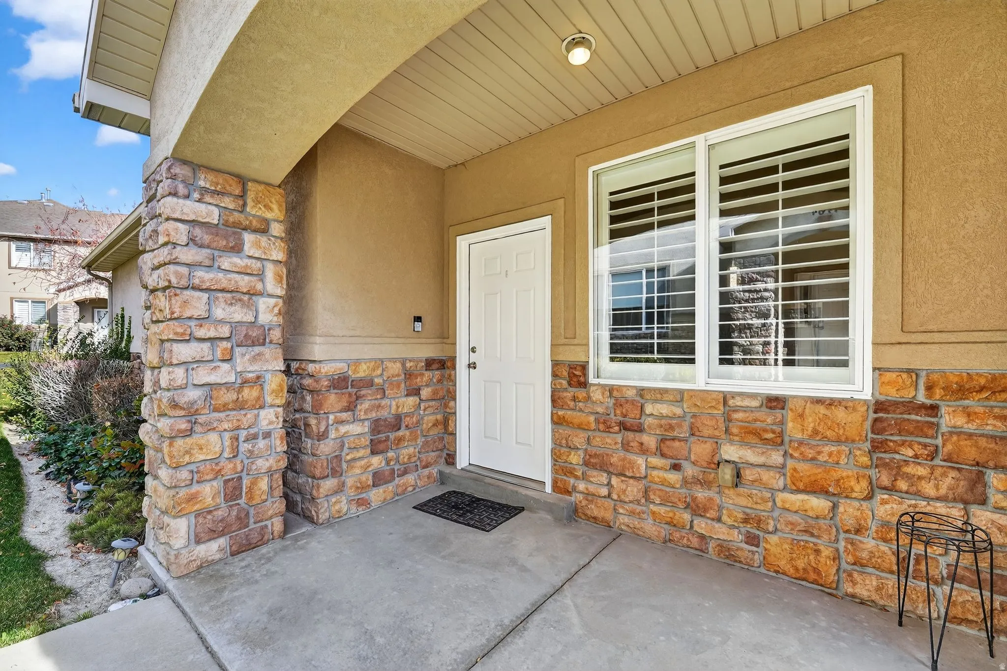 Covered porch entry featuring stone veneer accents, stucco siding, a white front door, and a multi-pane window with interior plantation shutters
