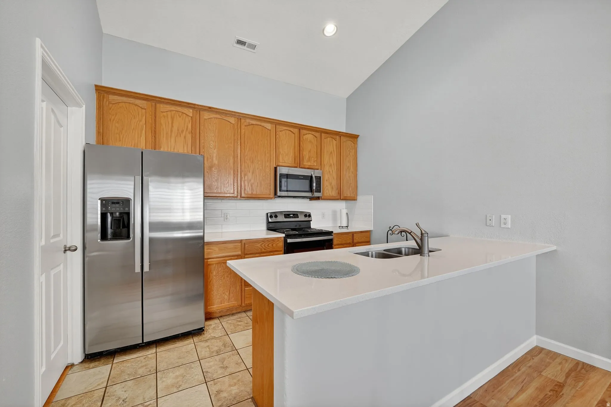 Kitchen featuring wood cabinetry, stainless steel appliances including a side-by-side refrigerator, white subway tile backsplash, and light-toned countertops