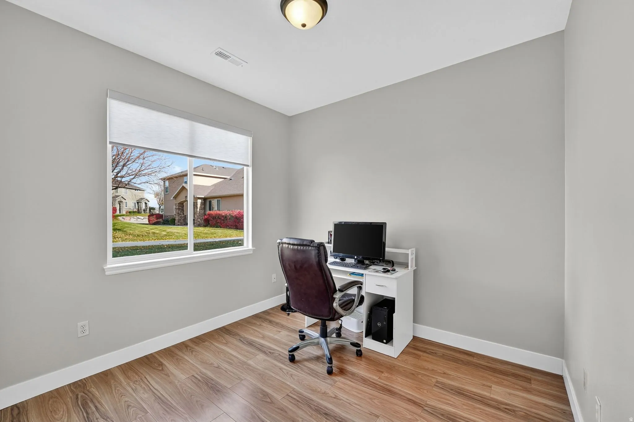 Bright room featuring wood-finish flooring, a large window with roller shades, white trim, and light grey walls