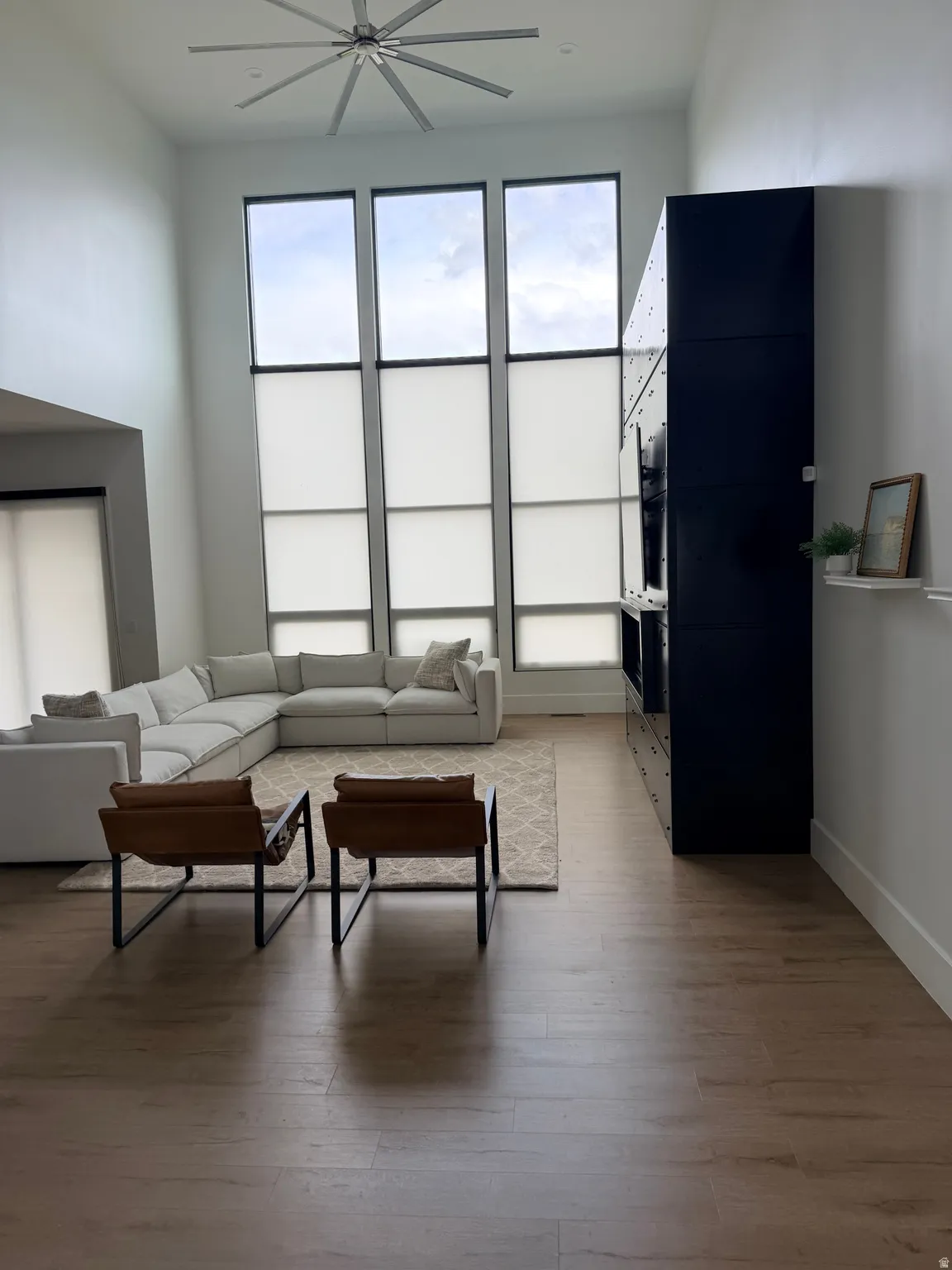High ceilings featuring a large ceiling fan and expansive windows with roller shades