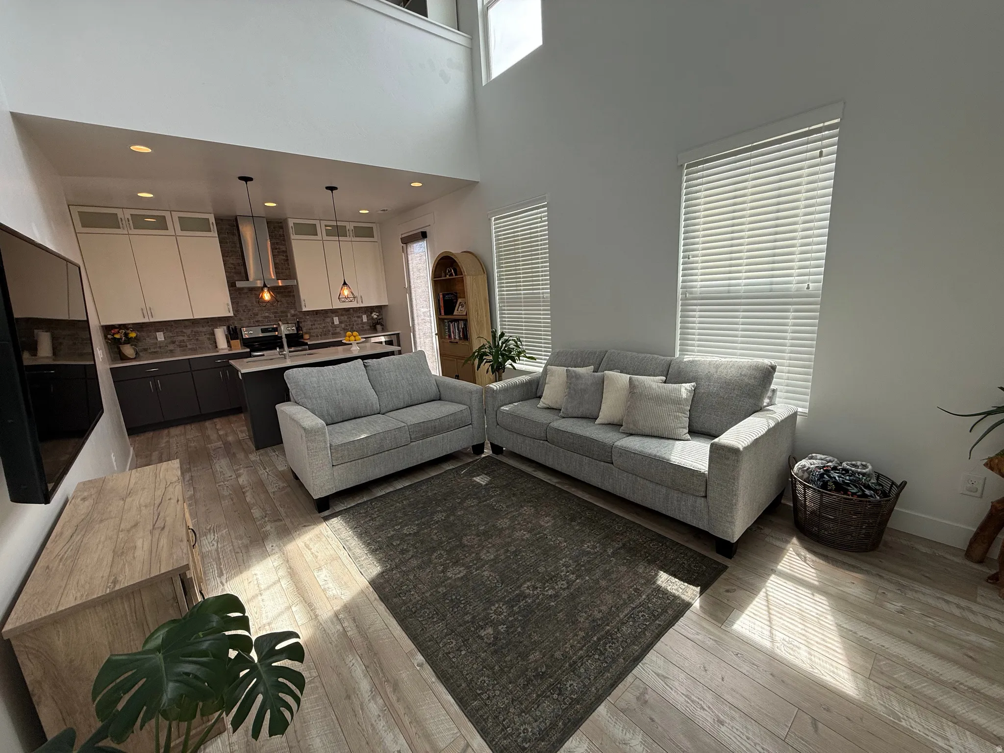 Open-concept living space featuring high ceilings, wood-finish flooring, and multiple windows with horizontal blinds
