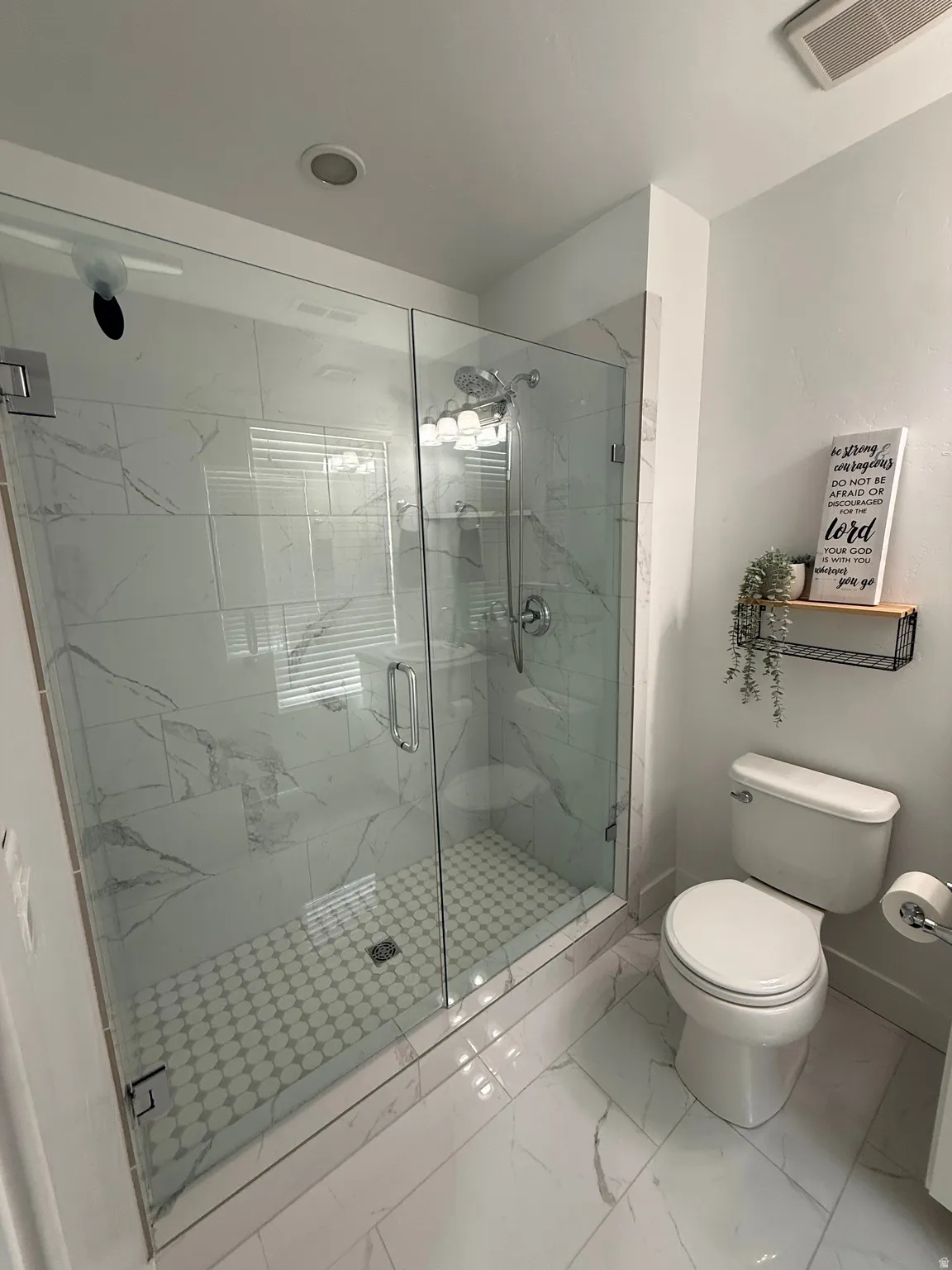 Glass-enclosed shower with white marble-look tile walls and a mosaic tile floor, complemented by coordinating marble-look floor tiles