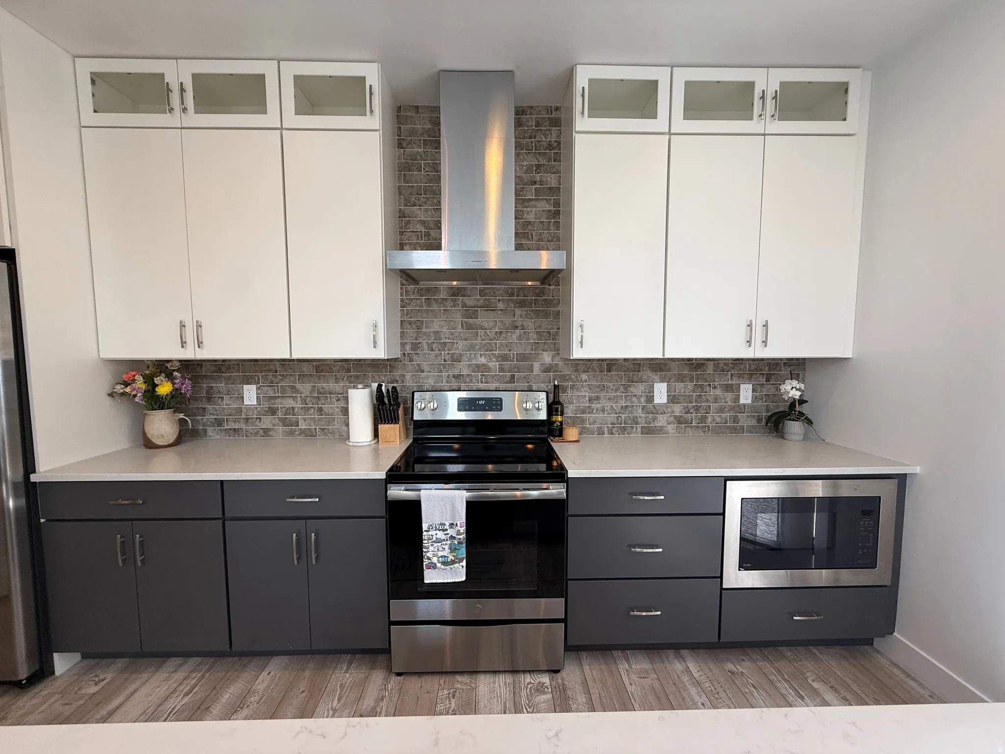 Modern kitchen featuring two-tone cabinetry, a stone-look backsplash, and wood-finish flooring
