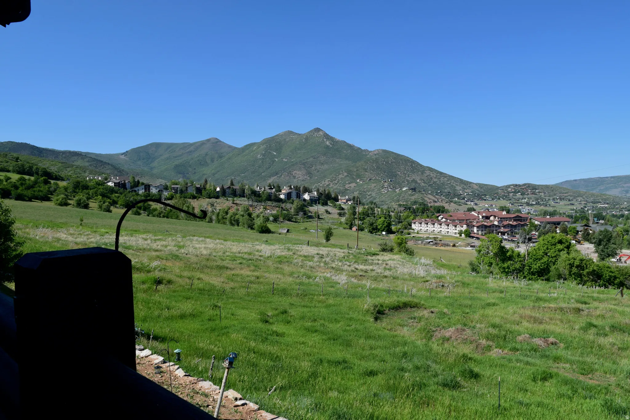 Expansive hillside panorama featuring verdant fields, distant mountain ranges, and scattered residential structures