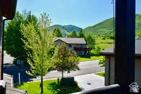 Property exterior featuring paved driveway, green lawn, mature trees, and a mountain backdrop