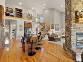 Open-concept interior featuring wood-finish flooring, a stone-clad fireplace, and a kitchen island with seating