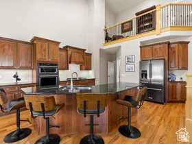 Spacious kitchen featuring an expansive center island with seating, dark stone countertops, wood cabinetry, built-in double ovens, and stainless steel appliances