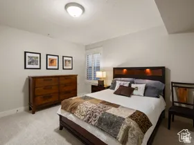Carpeted room featuring a window with white plantation shutters, a wood-finish dresser, and a dark wood headboard with integrated lighting
