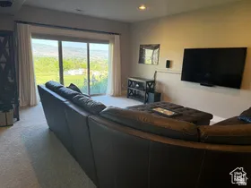 Sliding glass door opening to outdoor grounds, recessed lighting, wall-mounted television, wall-mounted audio speaker, and neutral-toned carpeting