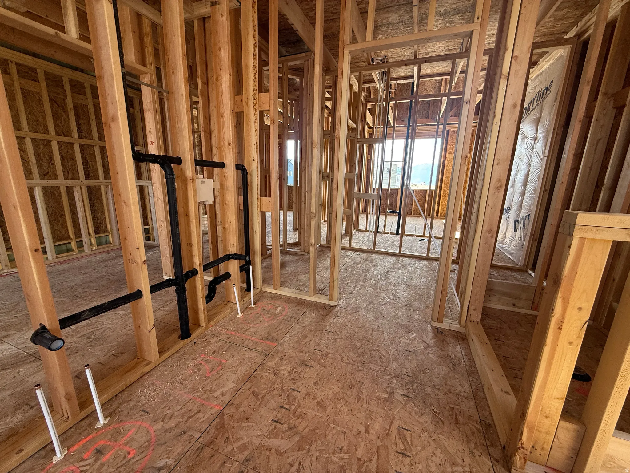 Interior framing showcasing engineered wood subflooring, visible plumbing rough-ins, and a window opening