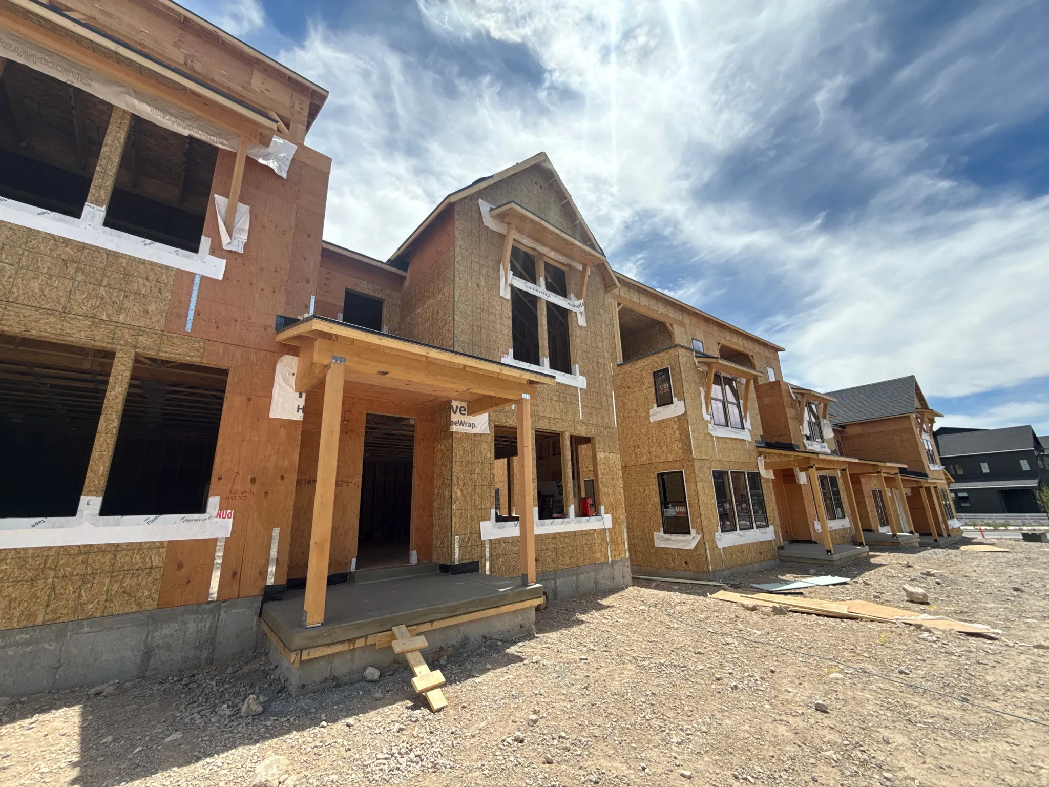 New construction row of residential properties with gabled rooflines, multiple window openings, and covered entryways