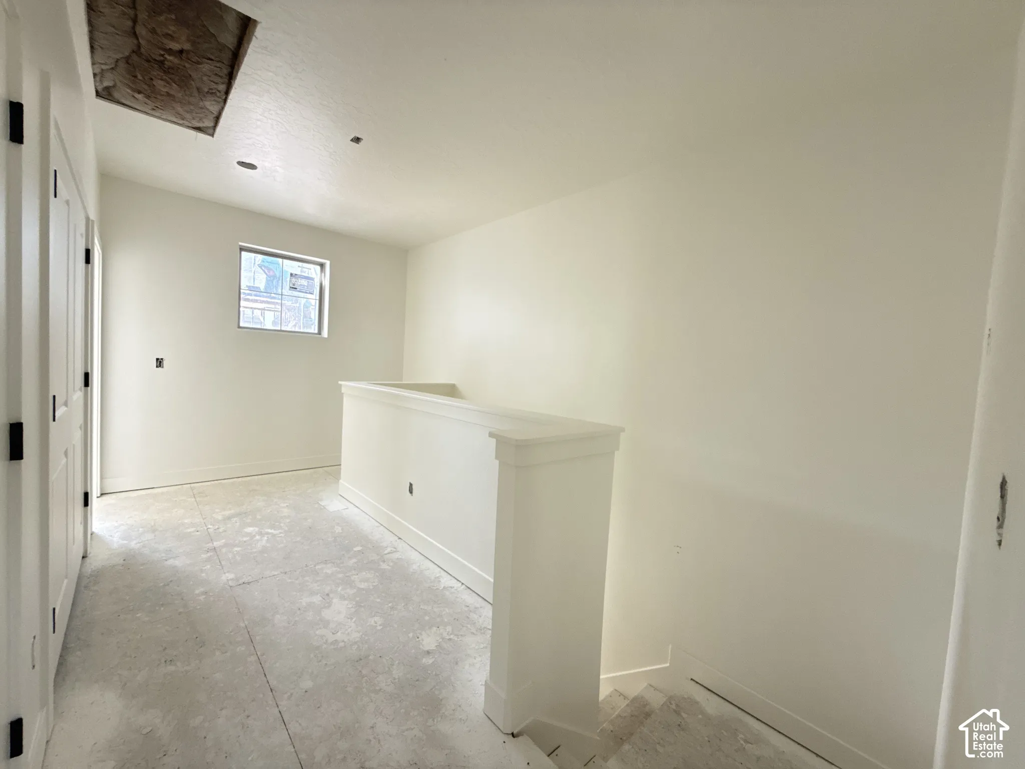 Painted interior walls, window with trim, white panel doors with black hardware, white railing, and unfinished flooring