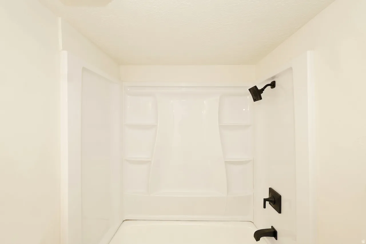 Bathtub-shower combination featuring a white surround with built-in shelving, matte black showerhead, and coordinating matte black faucet