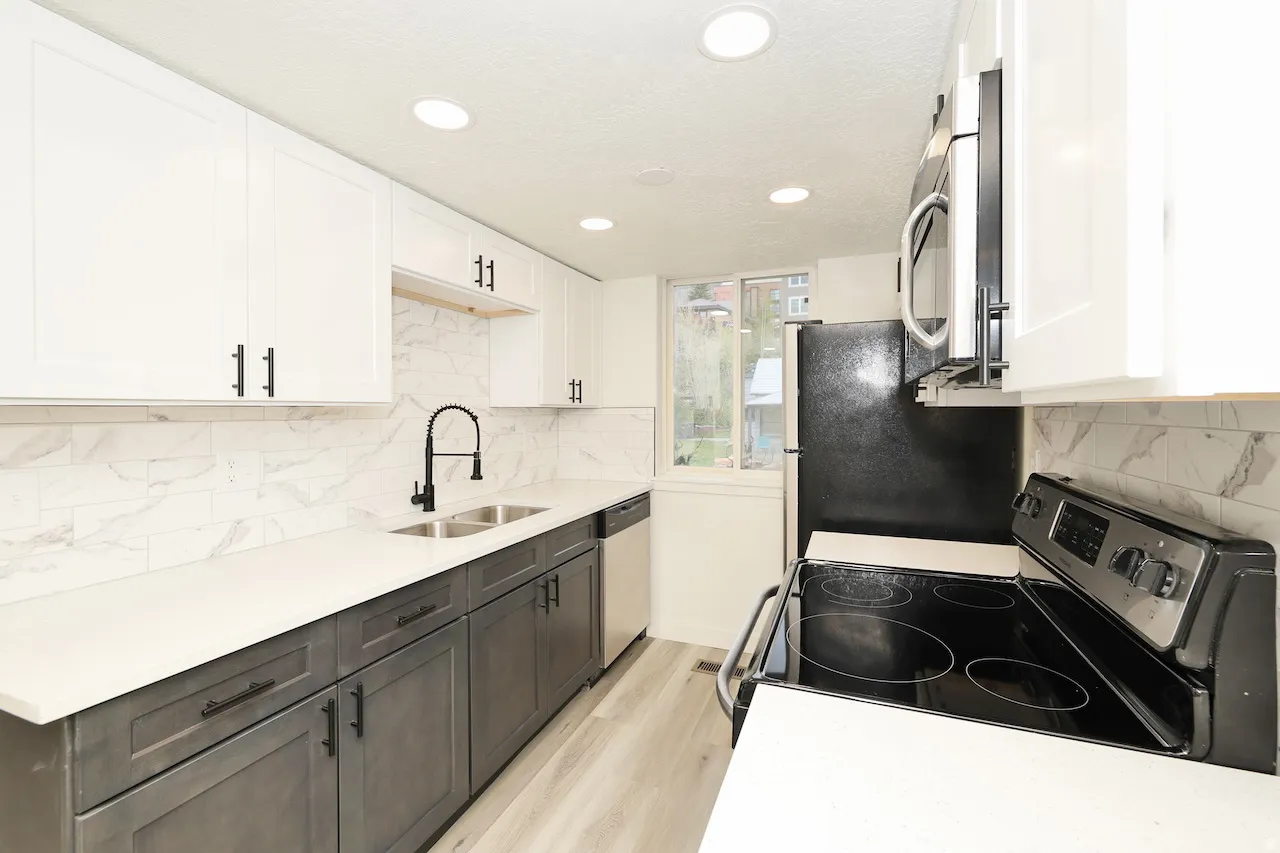 Contemporary kitchen featuring two-tone cabinetry, a dual-basin stainless steel sink with a matte black high-arch faucet, sleek white countertops, and a full tile backsplash