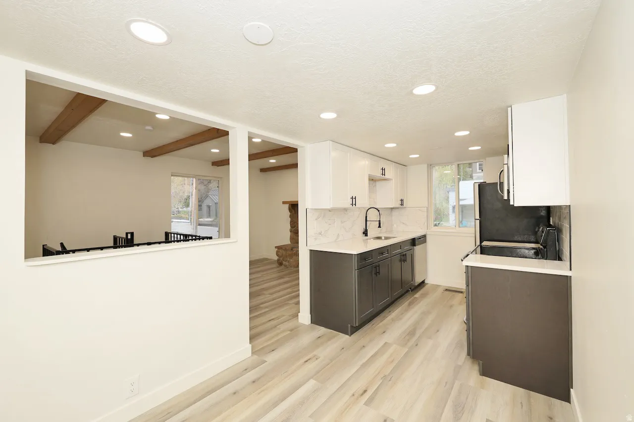 Modern kitchen featuring two-tone cabinetry, light wood-finish flooring, recessed lighting, a white quartz countertop, and a full tile backsplash