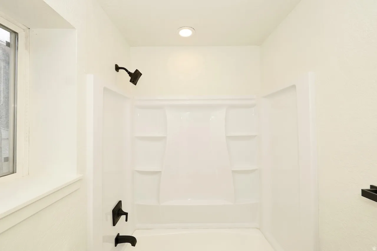 Bathtub and shower combination featuring a white surround, matte black fixtures, recessed lighting, and a window with white trim