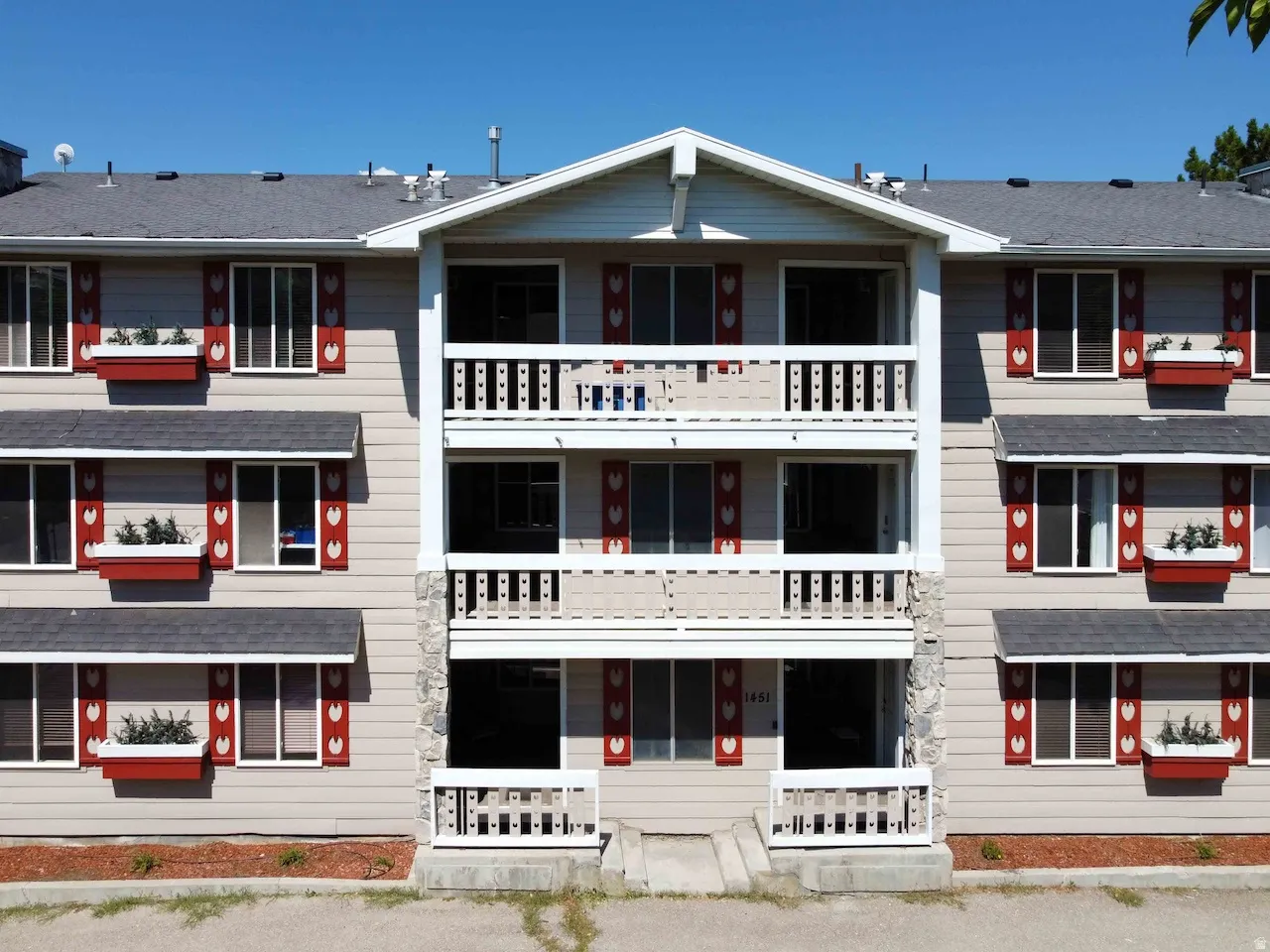 Multi-level building exterior featuring stone-clad columns, white baluster railings, and red window boxes