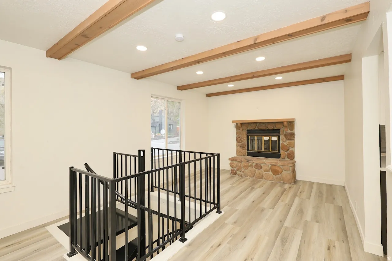 Living area featuring a stone fireplace, wood-finish flooring, recessed lighting, and exposed ceiling beams