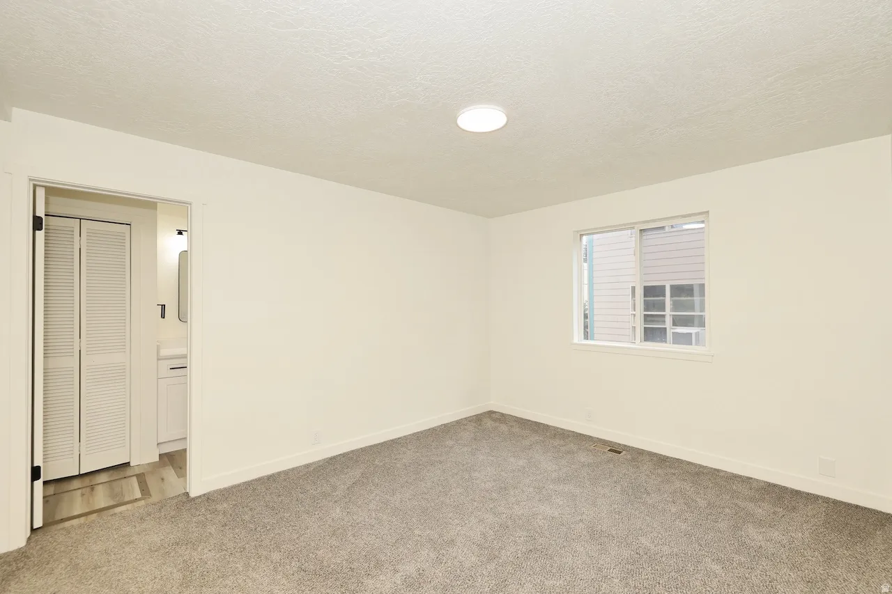 Neutral wall paint, gray carpet flooring, and a single window with white trim