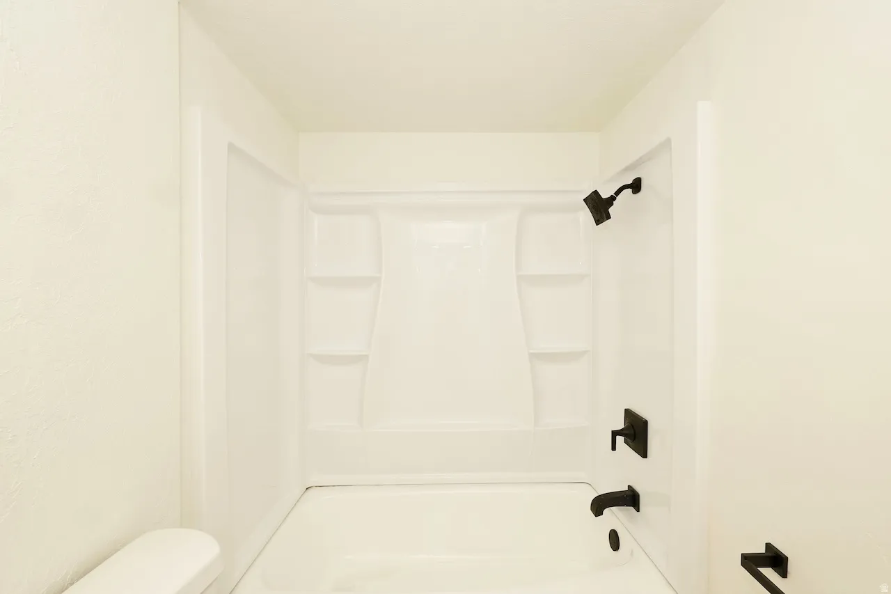 Bright white tub and shower combination featuring black fixtures, built-in shelving, and a modern aesthetic
