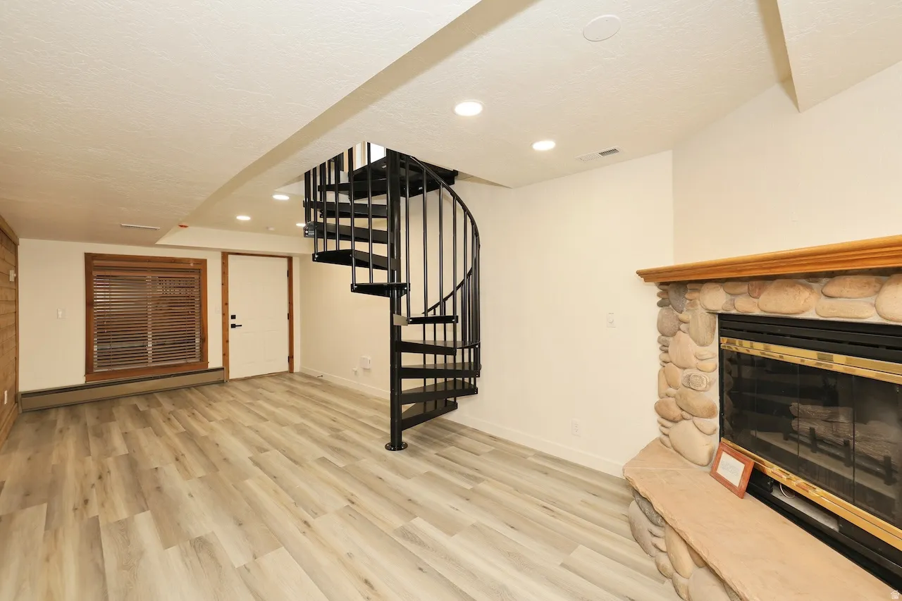 Spacious room featuring a spiral staircase, stone fireplace with hearth, wood-finish flooring, and recessed lighting