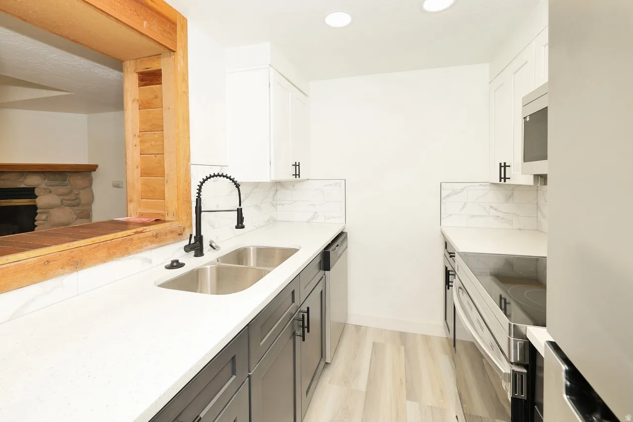 Contemporary kitchen featuring white shaker upper cabinetry and dark lower cabinetry, quartz countertops, a dual basin stainless steel sink with a matte black faucet, and a subway tile backsplash