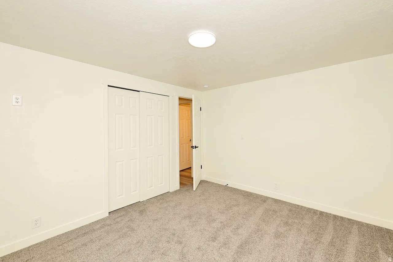Spacious room featuring neutral carpeting, light cream walls, white trim, a flush-mount ceiling light, and a bi-fold closet door