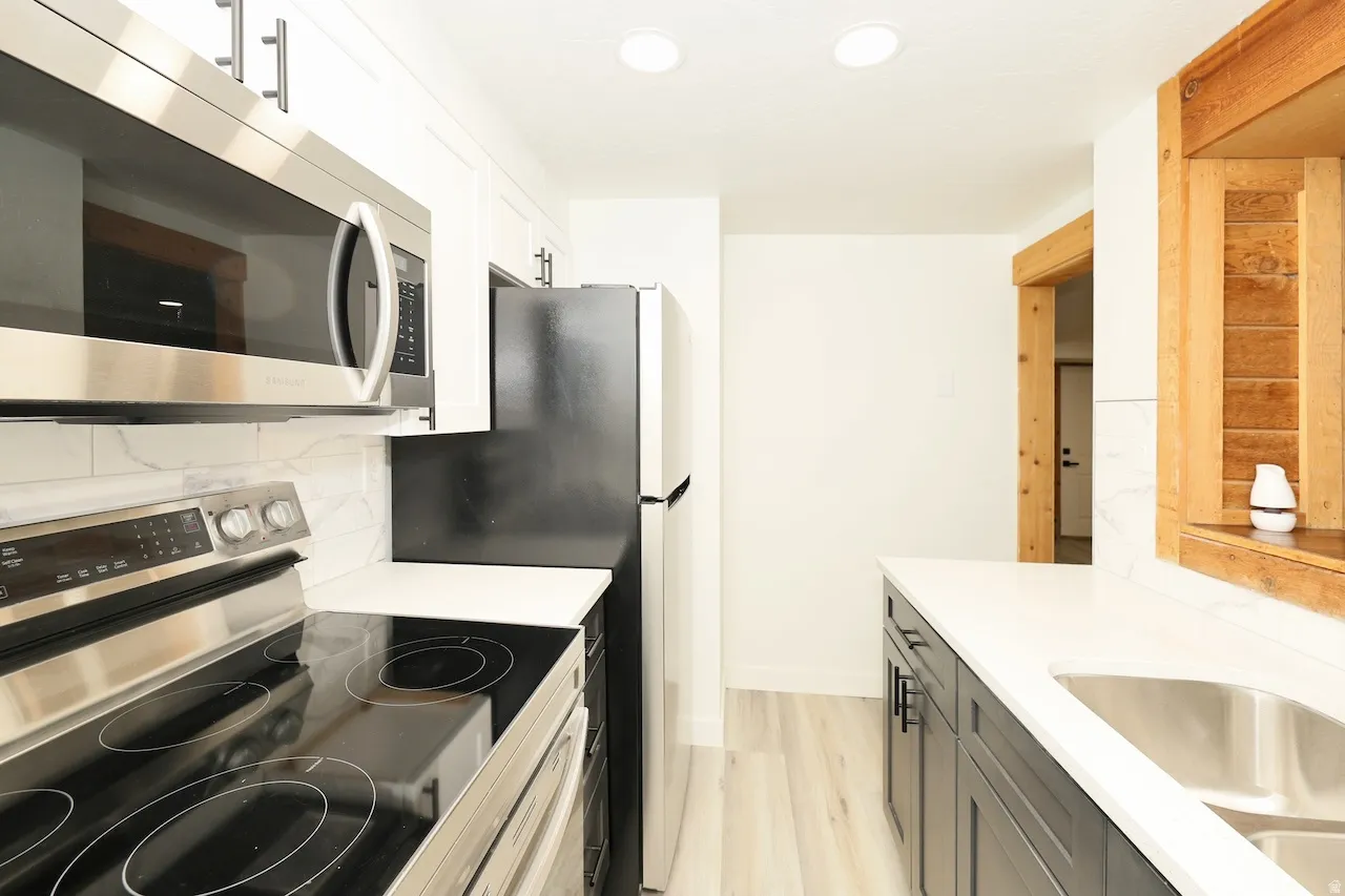 Contemporary kitchen featuring light wood-finish flooring, white countertops, and both white upper and dark lower cabinetry with black hardware