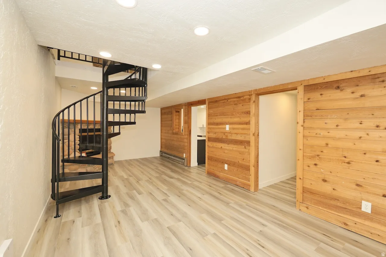 Open-concept room featuring a black metal spiral staircase, light wood-finish flooring, recessed lighting, and natural wood paneling with two sliding barn doors