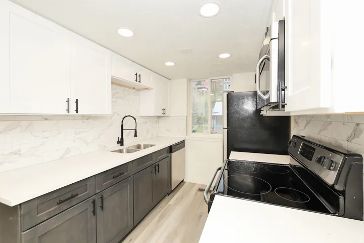Contemporary kitchen featuring two-tone cabinetry, a dual-basin stainless steel sink with a matte black high-arch faucet, sleek white countertops, and a full tile backsplash