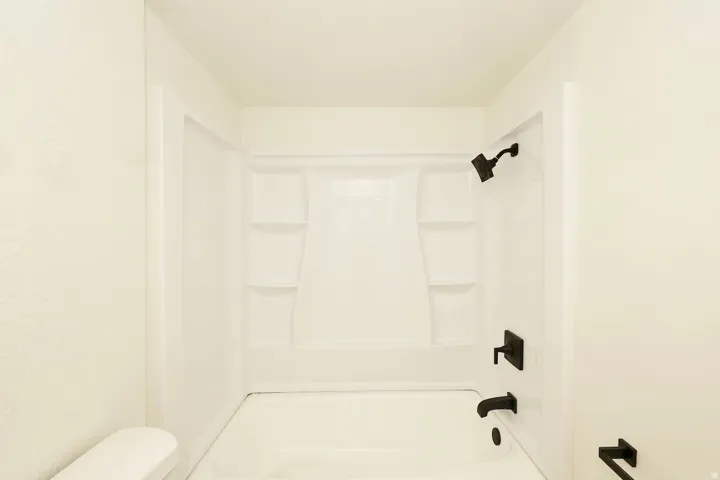 Bright white tub and shower combination featuring black fixtures, built-in shelving, and a modern aesthetic