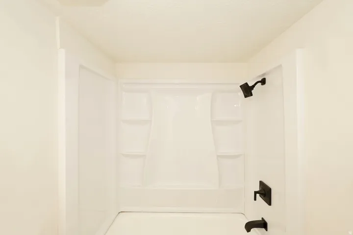 Bathtub-shower combination featuring a white surround with built-in shelving, matte black showerhead, and coordinating matte black faucet
