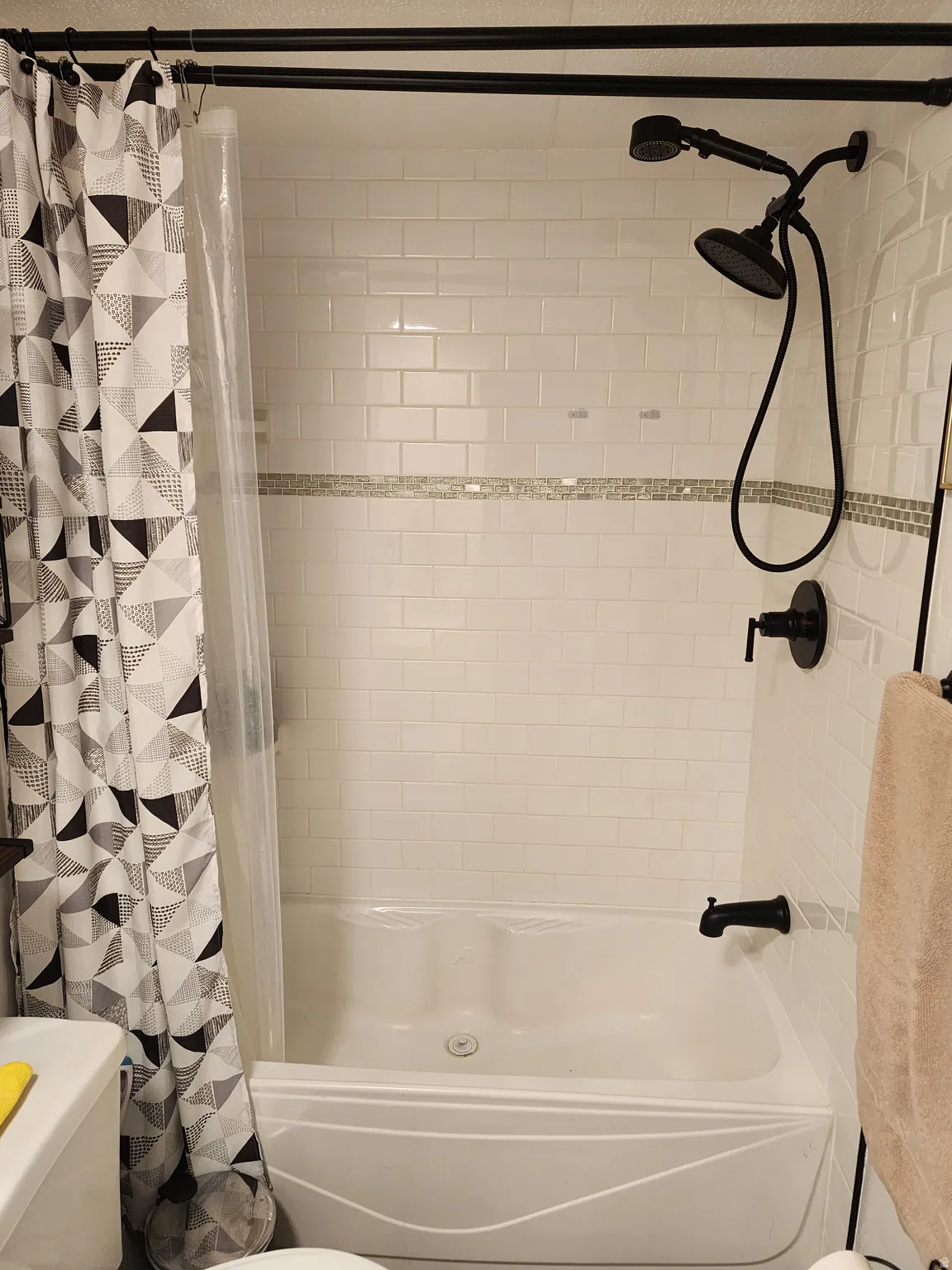 Tub and shower combination featuring subway tile surround with decorative accent band