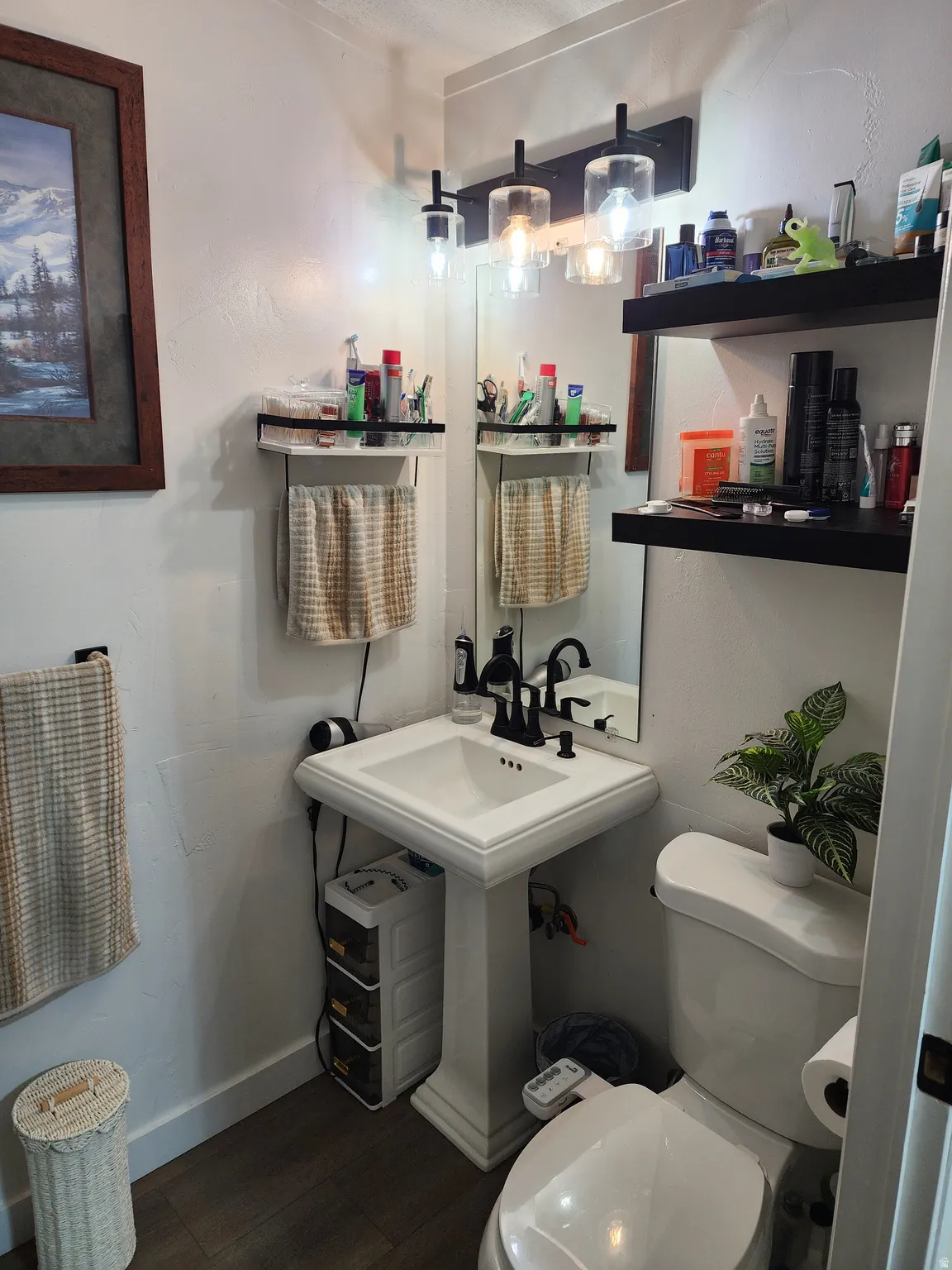 Pedestal sink with a black-finish faucet, mirror, and modern three-light vanity fixture