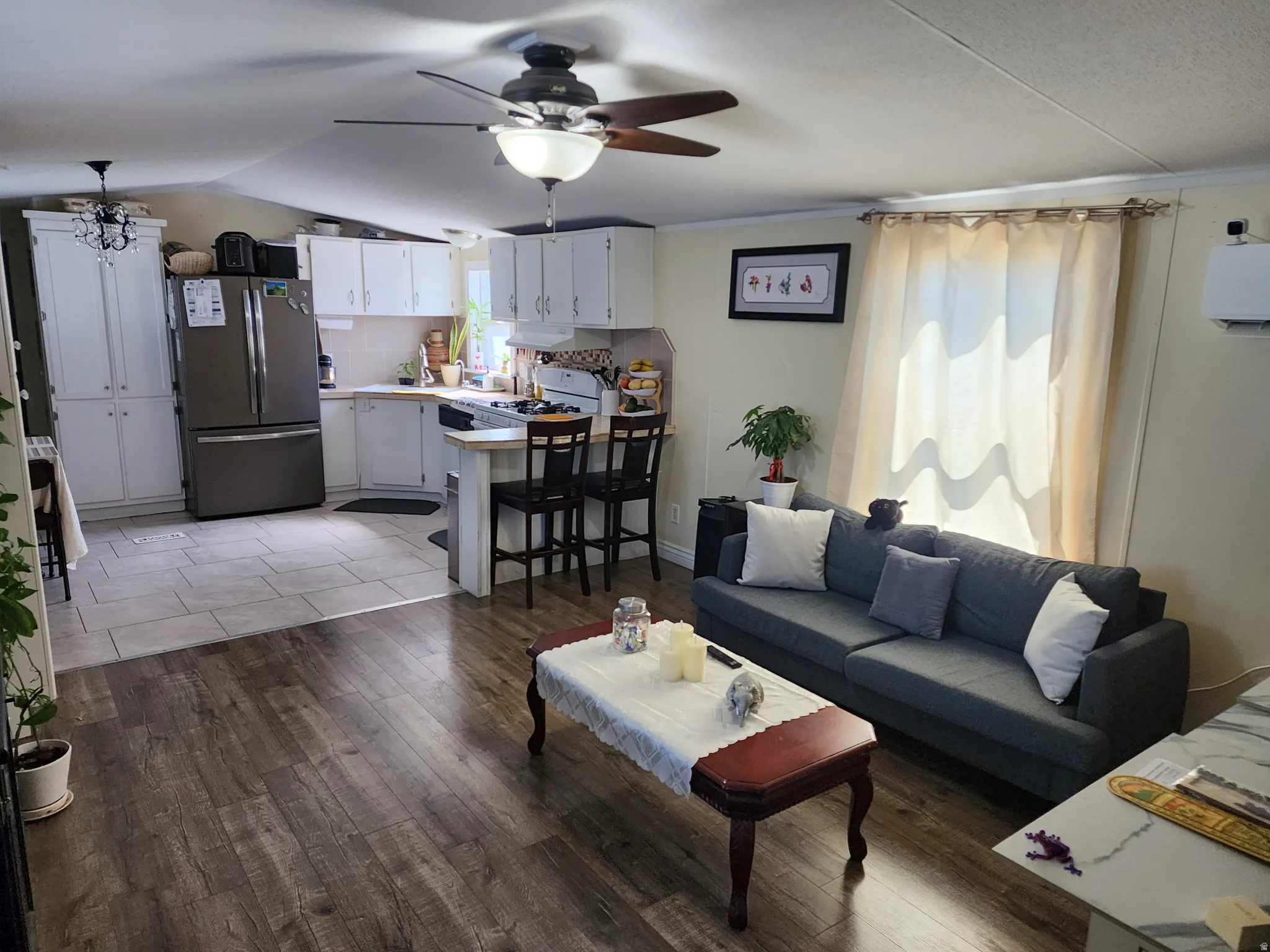 Open-concept living space featuring wood-finish flooring, a ceiling fan with integrated lighting, and a modern kitchen