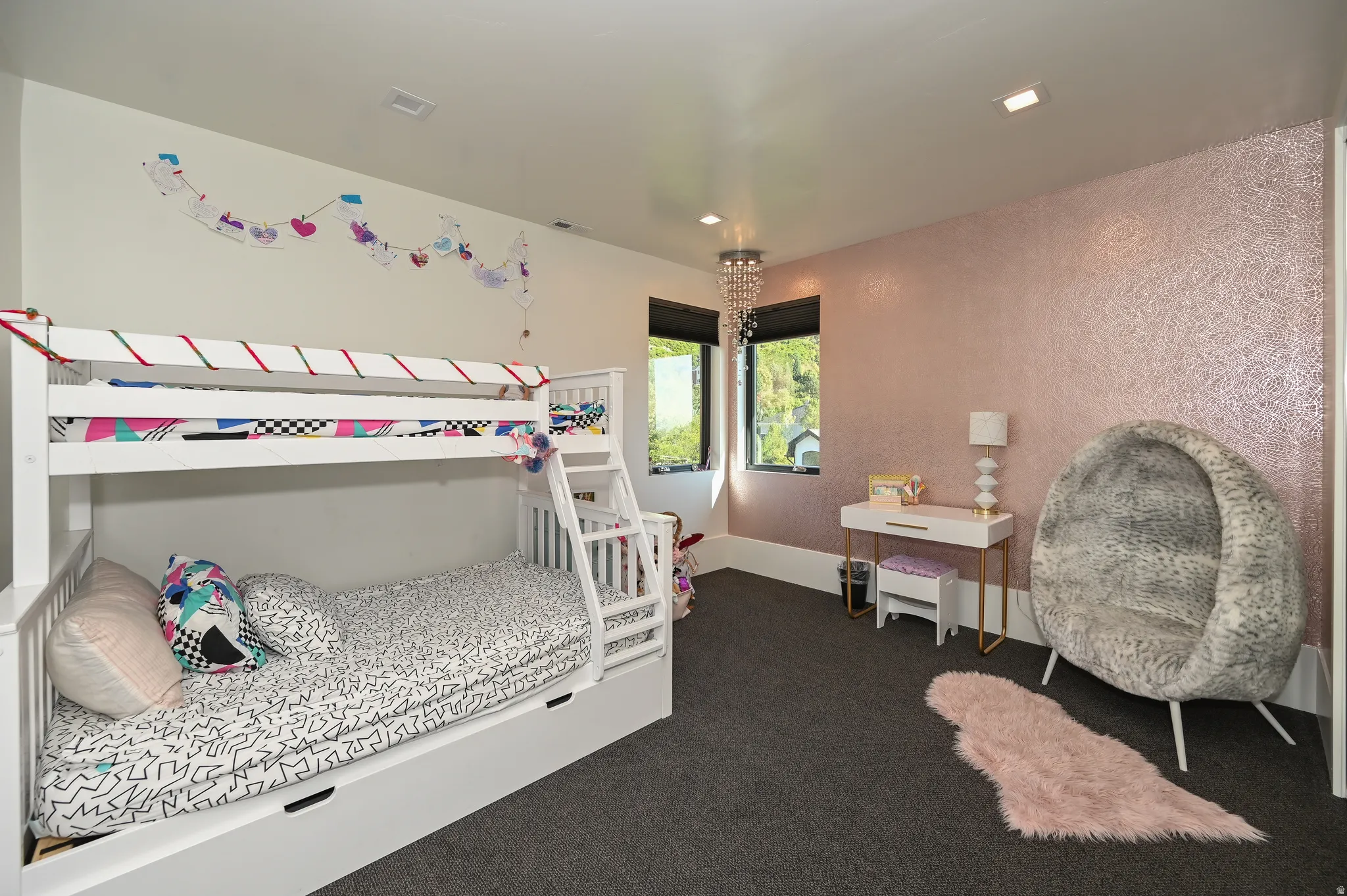 Recessed lighting illuminates a room featuring soft pink textured wallpaper, dark grey carpeting, and two windows