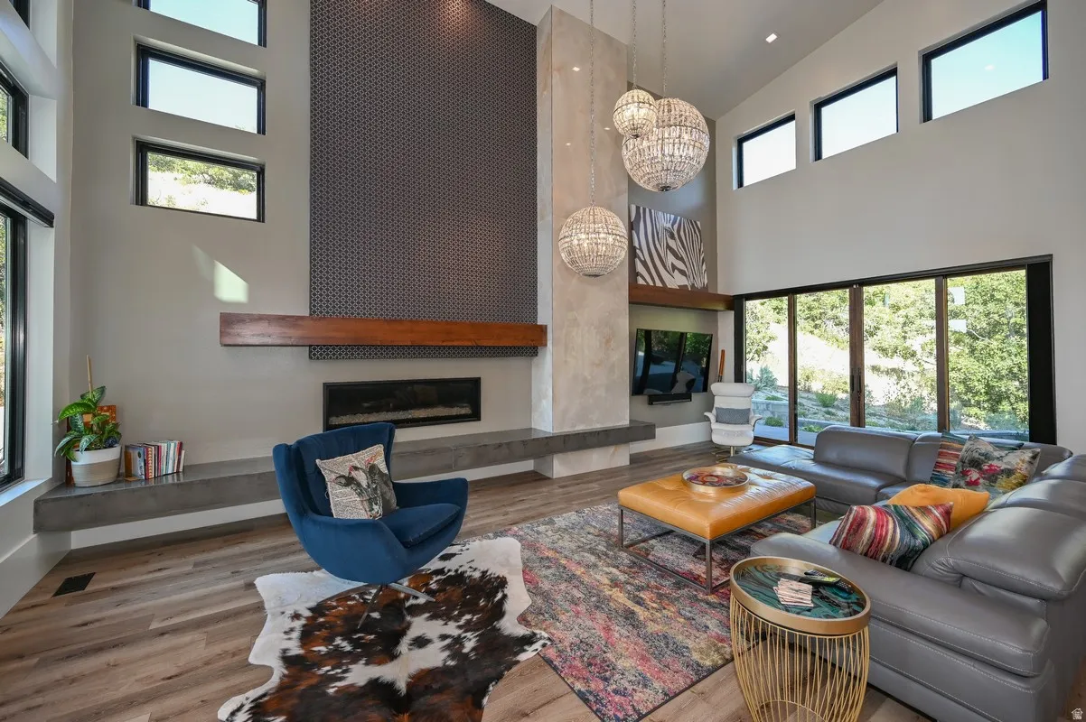Vaulted living space featuring wood-finish flooring, a linear fireplace with concrete hearth and wood mantle, a textured accent wall, and expansive glass sliding doors