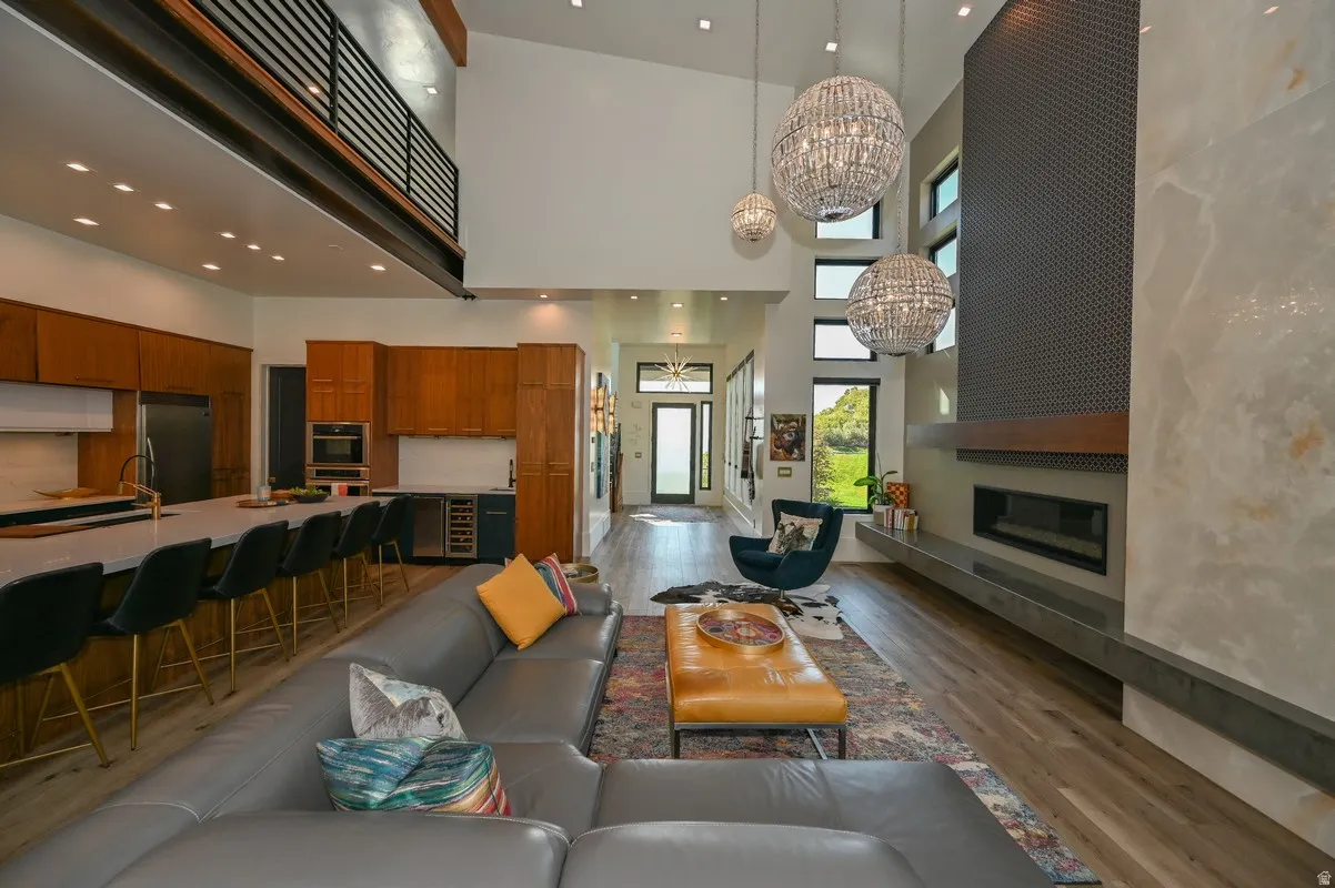 Spacious open-concept living area featuring high ceilings, wood-finish flooring, a contemporary fireplace with a long hearth, and a kitchen with an extended island