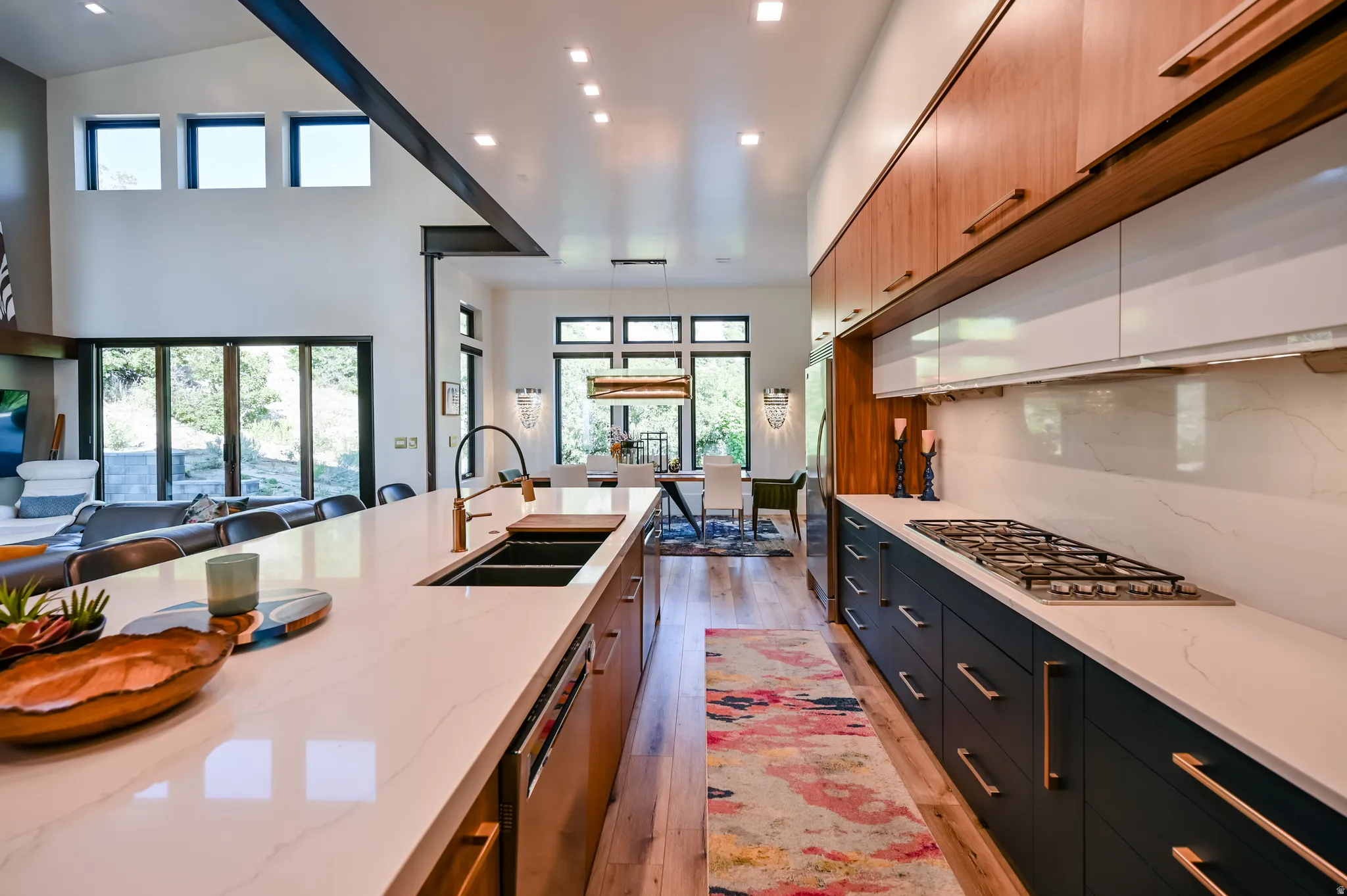 Modern kitchen featuring light wood-finish flooring, a long island with a built-in sink and gold-tone faucet, white countertops, and sleek cabinetry in both wood-tone and dark finishes