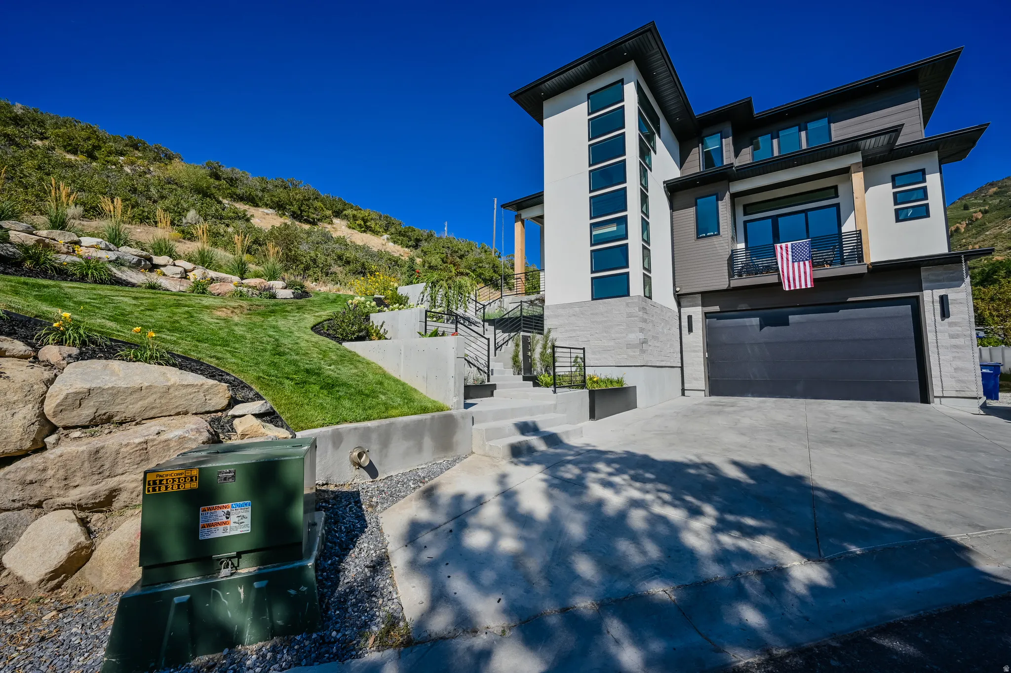 Modern multi-level exterior featuring a dark gray garage door, stacked stone accents, and a contrasting white facade