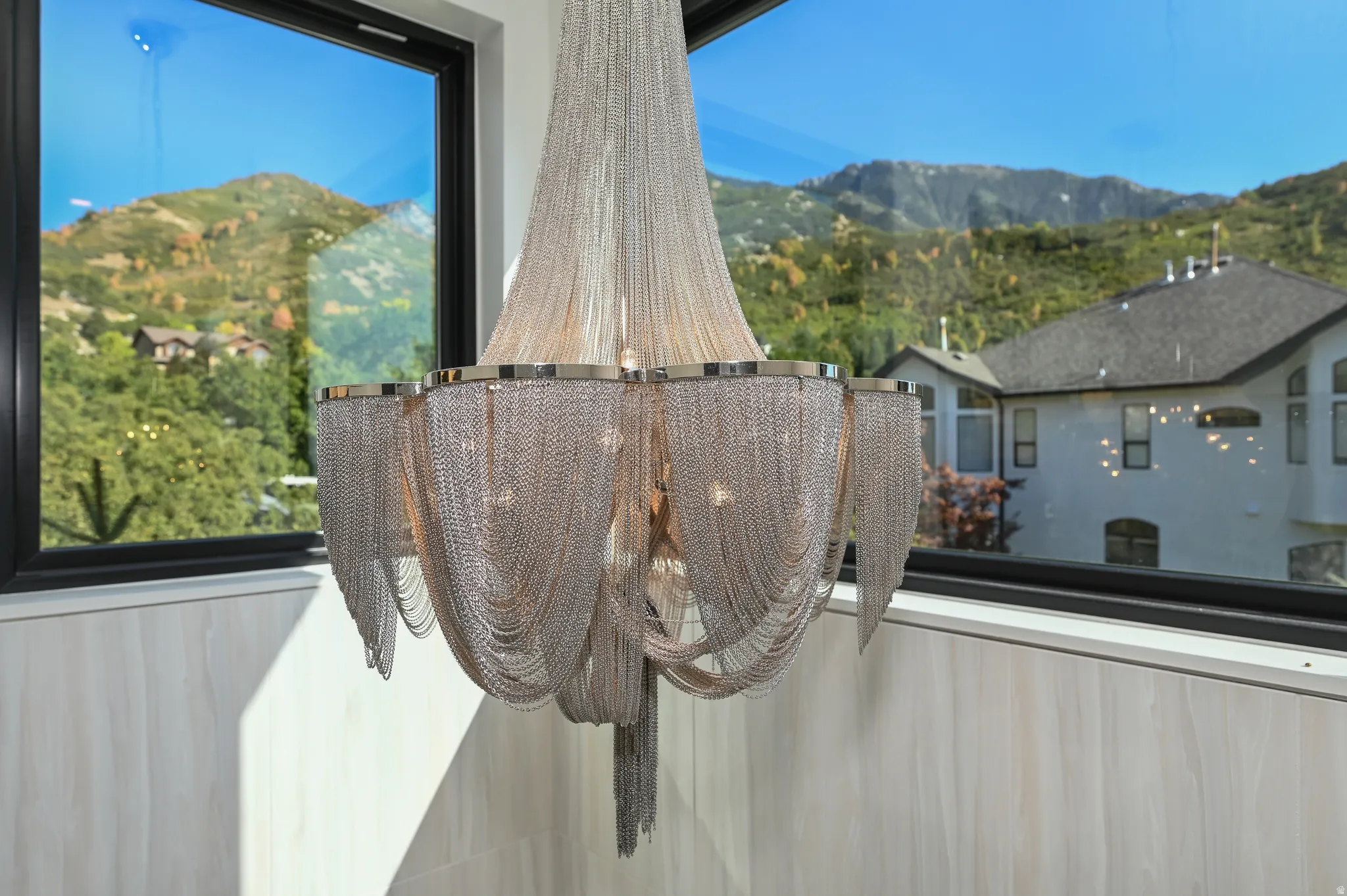Chain link chandelier with polished chrome accents, set against a backdrop of framed mountain scenery